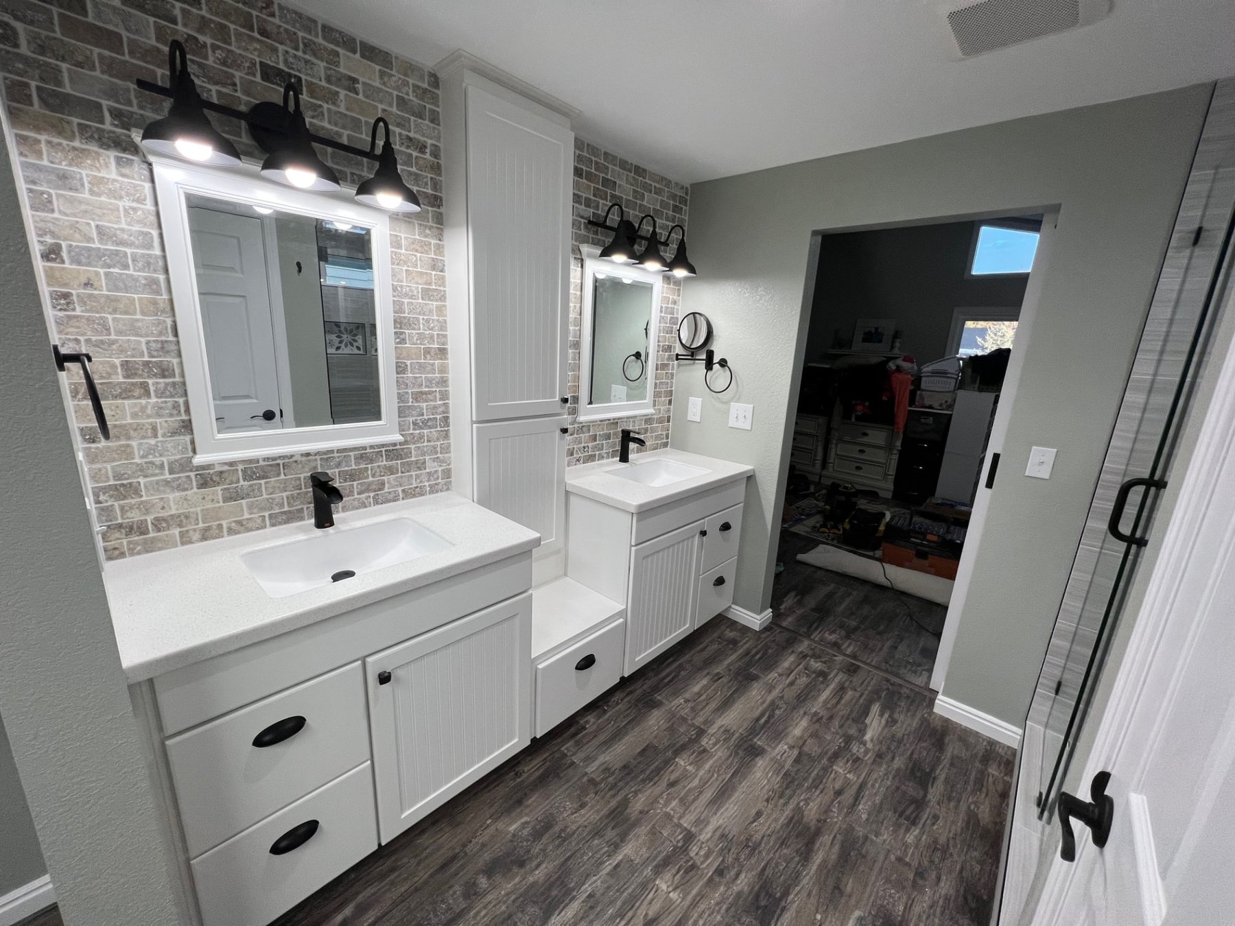 Twin white vanities with brick accent wall and black barn-style lighting